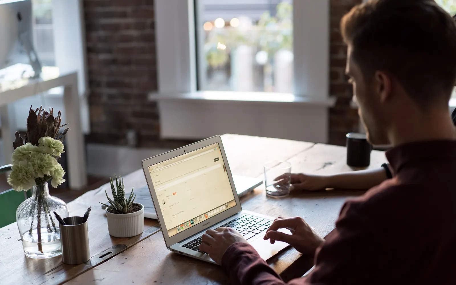Man working on a laptop at a wooden desk by a window